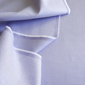 May include: Close-up of a light blue woven fabric with a textured pattern. The fabric is folded, revealing a white edge. The material has a subtle grid-like design, suitable for apparel or home decor.