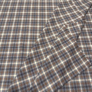 May include: Brown, navy, and white plaid fabric. The fabric is folded, showing the pattern's repeating squares. The plaid design is a classic pattern, suitable for various sewing projects, including apparel and home decor.