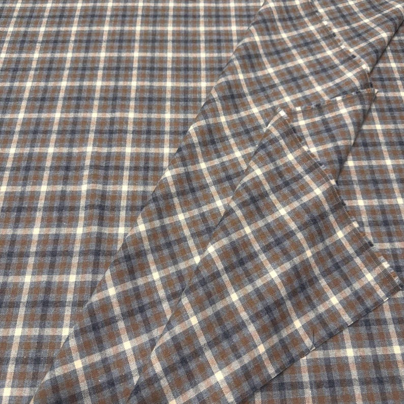 May include: Brown, navy, and white plaid fabric. The fabric is folded, showing the pattern's repeating squares. The plaid design is a classic pattern, suitable for various sewing projects, including apparel and home decor.