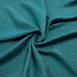 May include: Close-up of teal fabric with a textured, crinkled appearance. The material is draped and folded, creating shadows and highlights that emphasize the fabric's texture. The color is a deep, saturated teal, with a slight sheen.
