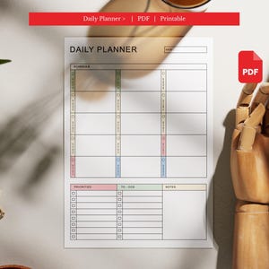 May include: A white daily planner with sections for schedule, priorities, to-dos, and notes. The planner has a PDF icon and the text "Daily Planner > | PDF | Printable". A wooden hand is in the background.