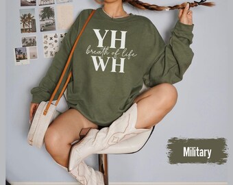 May include: An olive green sweatshirt with the text "YH breath of life WH" in white. The sweatshirt is part of a casual clothing collection. The image also shows a white purse with a brown strap and white cowboy boots.