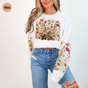 May include: White sweatshirt with a floral print on the front and sleeves. The flowers are in shades of pink, yellow, and green.