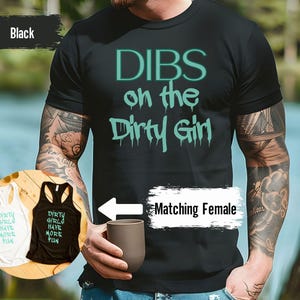 May include: Black t-shirt with the text "DIBS on the Dirty Girl" in teal lettering. The image also shows matching female tank tops in white and black, with the text "Dirty Girls Have More Fun".