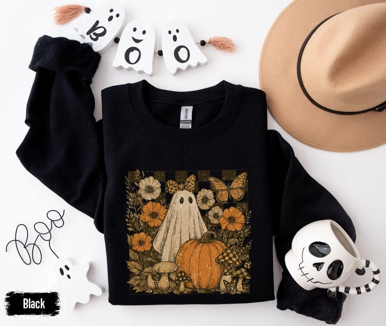 May include: Black crewneck sweatshirt featuring a vintage-style Halloween graphic. The design includes a ghost, pumpkin, flowers, and butterflies. The word "Boo" is written in cursive, and the word "Black" is in a black rectangle.