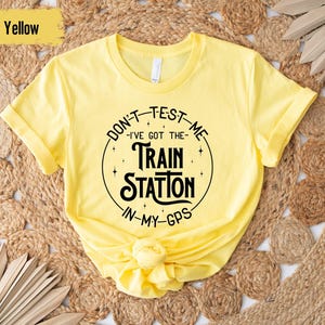 May include: Yellow t-shirt with a black graphic that says "Don't Test Me - I've Got The Train Station In My GPS".
