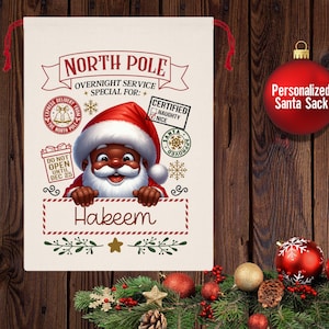 Könnte beinhalten: Ein personalisierter Weihnachtsmann-Sack mit rotem und weißem Streifenrand und einem festlichen Design. Der Sack zeigt einen Comic-Weihnachtsmann mit schwarzem Gesicht, weißem Bart und roter Mütze. Der Sack ist mit "North Pole Overnight Service Special For: Hakeem" beschriftet.