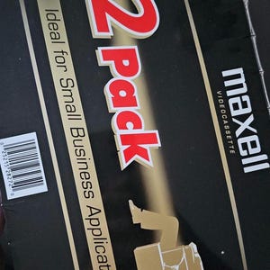 May include: A black and gold box with the text "12 pack" in red and white. The box also says "Ideal for Small Business Applications" and "maxell videocassette".