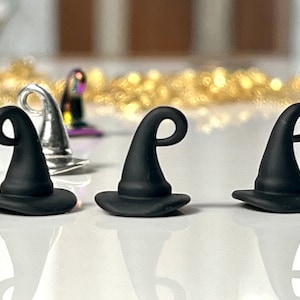 May include: Three black witch hats with a pointed top and a curled brim. The hats are made of a smooth, matte material.