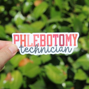 May include: A rectangular sticker with the words "PHLEBOTOMY technician" in red and gray lettering. The sticker is held against a backdrop of green foliage.