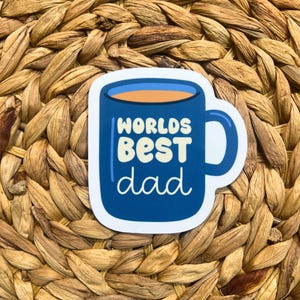 May include: A blue coffee mug sticker with the text "Worlds Best Dad" in yellow and white lettering.