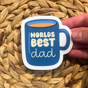 May include: A blue coffee mug sticker with white text that reads "Worlds Best Dad".