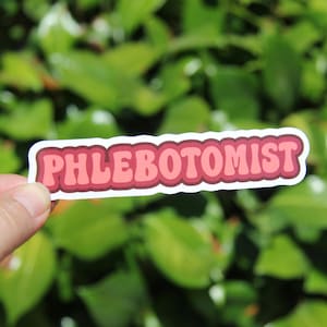 May include: A sticker with the word "PHLEBOTOMIST" in a retro font. The text is in shades of pink and red, outlined in white. The sticker is held against a backdrop of green foliage.