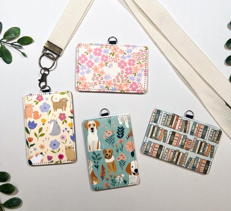 Op de afbeelding: Vier rechthoekige ID-badgehouders met verschillende ontwerpen. E&eacute;n heeft een bloemenpatroon, een andere heeft katten, een derde heeft honden en de laatste heeft een boekenplankenpatroon. Ze zijn bevestigd aan een cr&egrave;mekleurig koord.