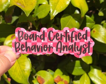 May include: A die-cut sticker featuring a pink and light pink checkered pattern with small white star accents. The text Board Certified Behavior Analyst is printed in a bold black script font across the center of the sticker.
