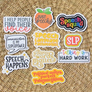 May include: A collection of colorful stickers with speech therapy-related phrases. The stickers feature text like "Speech Squad," "Communication is my superpower," and "Talking is hard work." The stickers are on a woven, tan background.