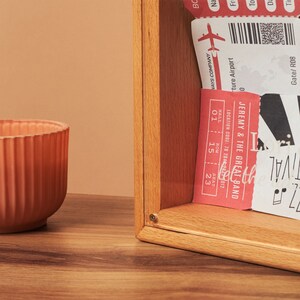 May include: A wooden box with a collection of tickets and a ribbed orange bowl. The tickets are red and white, with text that reads "JEREMY & THE GREAT BAND" and "VAYS COMPANY". The bowl is on a wooden surface.