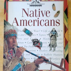 May include: A book cover with a colourful design featuring a Native American man holding a pipe. The title of the book is "Native Americans" and the subtitle is "The Nature Company Discoveries Library".