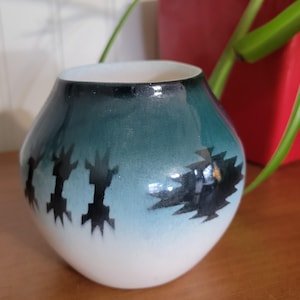 May include: A small, round, white ceramic vase with a teal glaze and black geometric designs. The vase has a smooth, glossy finish.