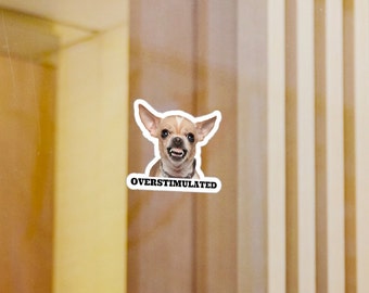 May include: A sticker featuring a chihuahua with a snarling expression. The sticker has the text "OVERStimulated" below the image.