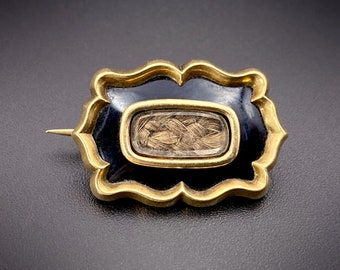 May include: A gold-toned brooch with a black enamel border and a glass locket containing a braid of hair.