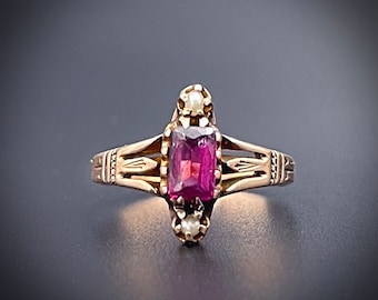 May include: A gold ring with a pink gemstone and two small white pearls on either side.