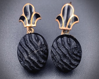May include: A pair of black and gold earrings with a textured round design and a decorative top.