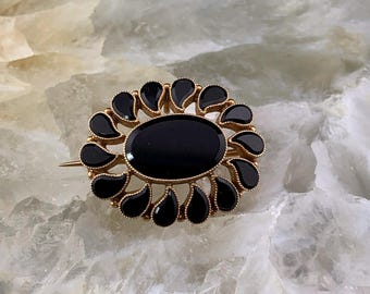 May include: A gold brooch with a black onyx centre surrounded by a ring of smaller black onyx stones.