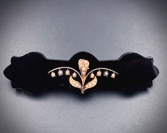 May include: A black jet brooch featuring a gold lily of the valley design with pearl accents.