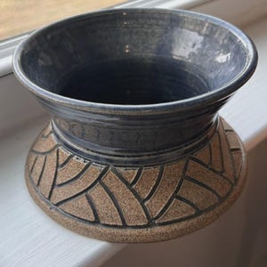 May include: A handcrafted ceramic vase with a wide, dark blue rim and a textured, brown base. The base features a woven pattern design. The vase is a decorative item, suitable for displaying flowers or as a standalone art piece.