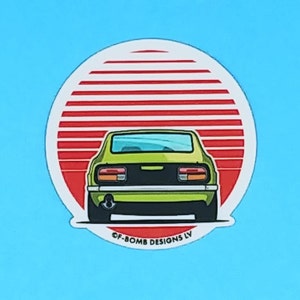 May include: A green vintage car driving into a red and white sunset. The car is a rear view of a classic Japanese sports car. The sticker has the text "GF-BOMB DESIGNS LV" at the bottom.