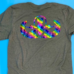 May include: A dark green t-shirt with a rainbow colored bomb and wings design on the back. The design is a military-style patch.