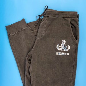 May include: Dark gray sweatpants with a silver EOD badge and the text "EOMFD" printed on the right leg.