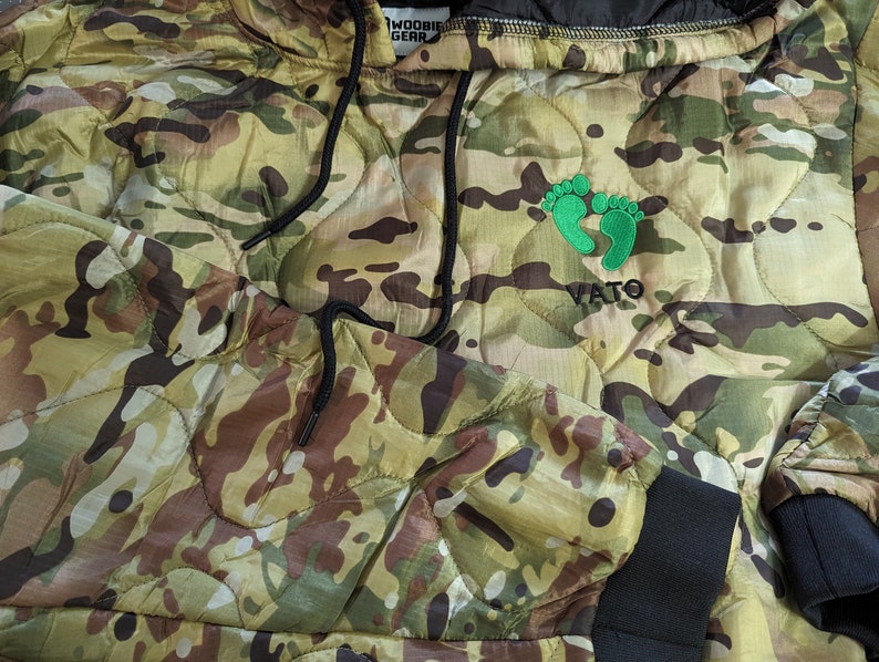 May include: Camouflage hooded jacket with a green footprint logo and the word "VATO" embroidered on the front.