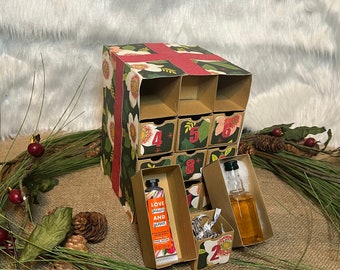 May include: A brown cardboard advent calendar with 12 drawers decorated with a floral pattern and a red ribbon. The drawers are numbered 2, 4, 5, 6, and 8. The calendar is open and reveals a small bottle of liquid and a tube of hand cream.