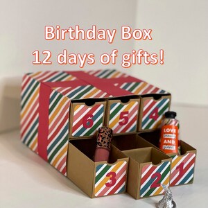 May include: A colorful cardboard box with drawers numbered 1 through 6. The box is decorated with stripes and has a red ribbon. The drawers contain small gifts, including a bottle of lotion, a tube of lipstick, and a chocolate kiss.