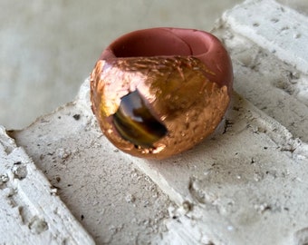 May include: A ring made of terracotta clay with a gold-leaf finish and a tiger's eye stone in the center.