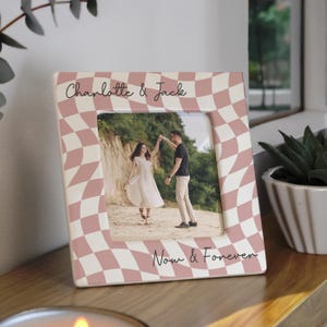 May include: A ceramic photo frame with a pink and white chequered pattern. The frame holds a photo of a couple dancing. The text "Charlotte & Jack" and "Now & Forever" are written on the frame.