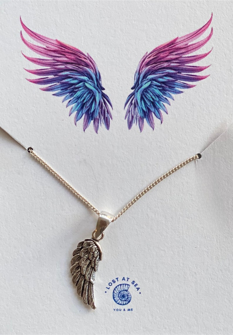 May include: A silver necklace with a single angel wing pendant. The necklace is on a white background with a pair of watercolor wings in the background. The text "Lost at Sea. You & Me" is printed below the necklace.