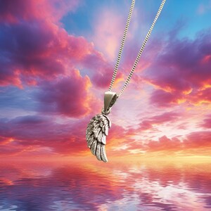 May include: A silver chain necklace with a detailed silver wing pendant. The necklace is hanging against a backdrop of a colorful sunset sky and a reflective body of water.