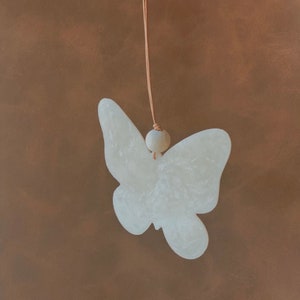 May include: A white ceramic butterfly ornament hanging from a brown cord with a white bead.
