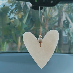 May include: A white heart-shaped car air freshener with a brown string and wooden beads hanging from the rearview mirror of a car.