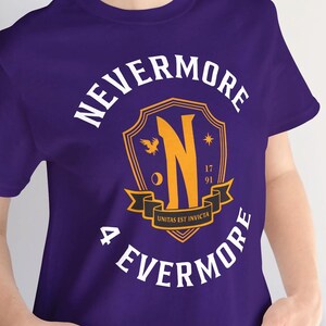 May include: A purple t-shirt with the words "NEVERMORE" and "4 EVERMORE" in white, surrounding a gold and black crest with the letter "N". The crest also includes the words "UNITAS EST INVICTA" and the numbers "17" and "91".