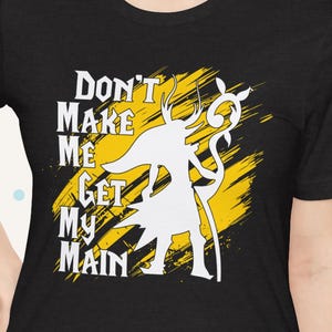 Może przedstawiać: Czarna koszulka z białą grafiką postaci trzymającej laskę na żółtym tle. Tekst "DON'T MAKE ME GET MY MAIN" jest wydrukowany na biało. Koszulka ma krótkie rękawy i okrągły dekolt.