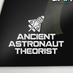 May include: A white vinyl sticker with a stylized rocket ship and the text "ANCIENT ASTRONAUT THEORIST" on a black background. The sticker also includes the text "LF1M LOOKING FOR ONE MORE" in the top right corner.