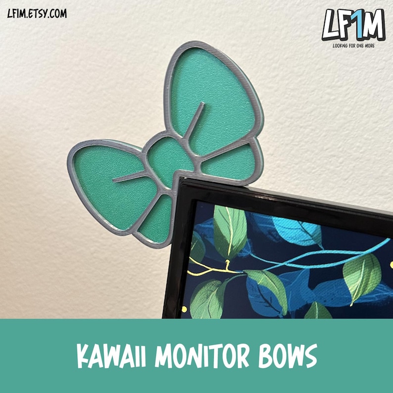 May include: A teal bow-shaped monitor accessory with a silver outline, positioned on the top corner of a computer monitor. The monitor displays a nature scene with green leaves and blue accents. The text "KAWAII MONITOR BOWS" is at the bottom.