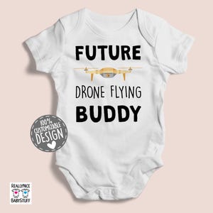 May include: White baby bodysuit with black text that reads "Future Drone Flying Buddy". A cartoon drone is pictured above the text.