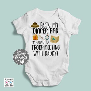 May include: White baby bodysuit with a black and white graphic design. The graphic features a camping scene with a campfire, compass, map, and a hat. The text reads "Pack My Diaper Bag I'm Going To Troop Meeting With Daddy!"