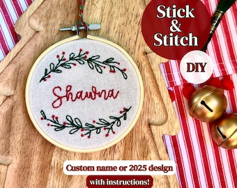 May include: Embroidered hoop art with the name "Shawna" in red script, surrounded by green leaves and red berries. The text "Stick & Stitch" and "DIY" are visible. The wooden background is shaped like a Christmas tree.