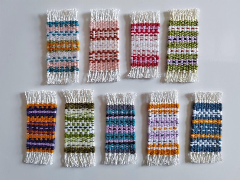 May include: Ten small woven wall hangings with fringe. The hangings are in various colors and patterns, including red, white, blue, green, purple, and orange.